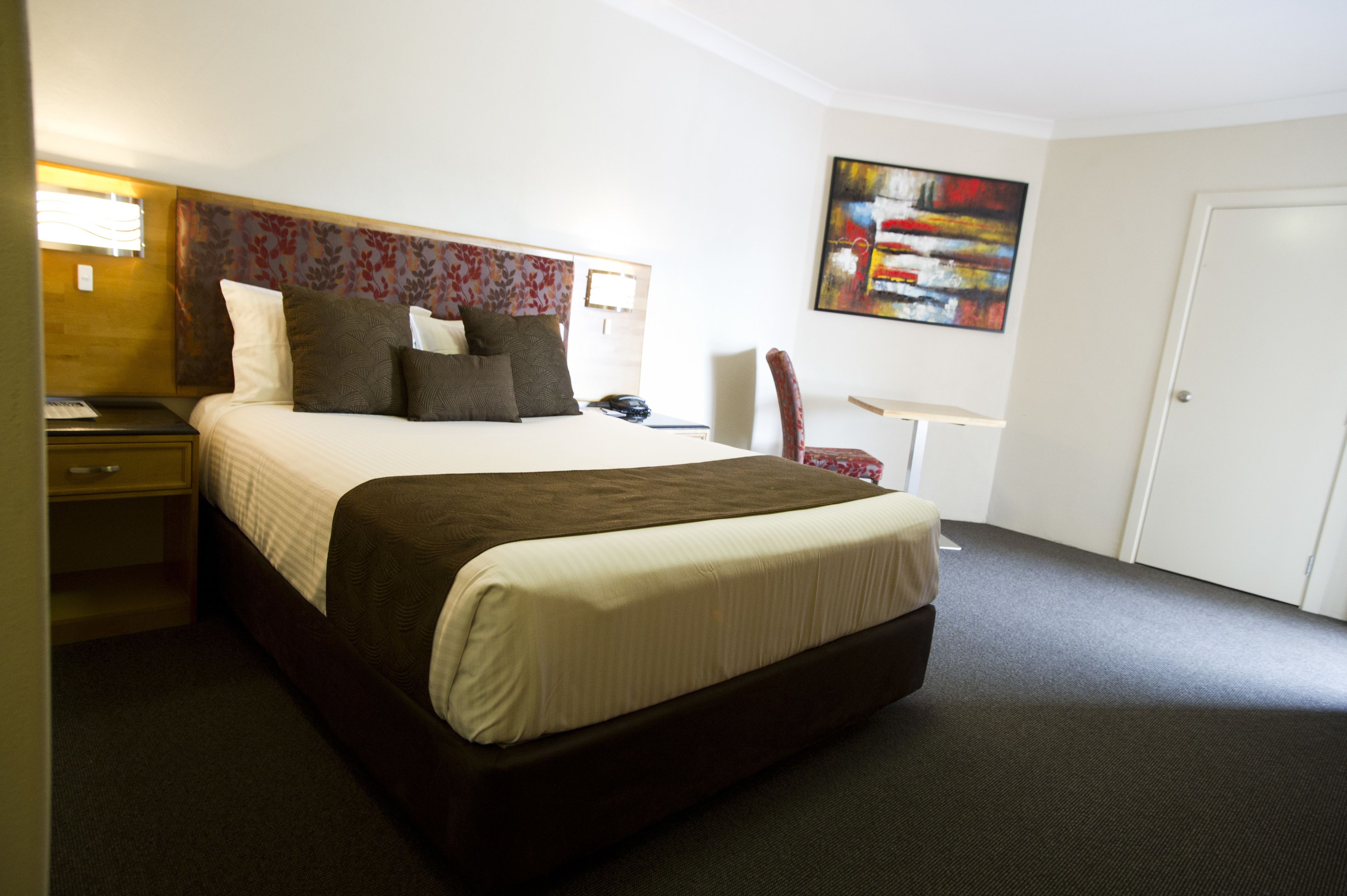 A hotel room with a large bed, a desk, a chair, and a painting on the wall.