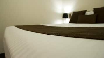 A neatly made bed with a white and brown bedspread, a black lamp on a bedside table, and a white wall in the background.