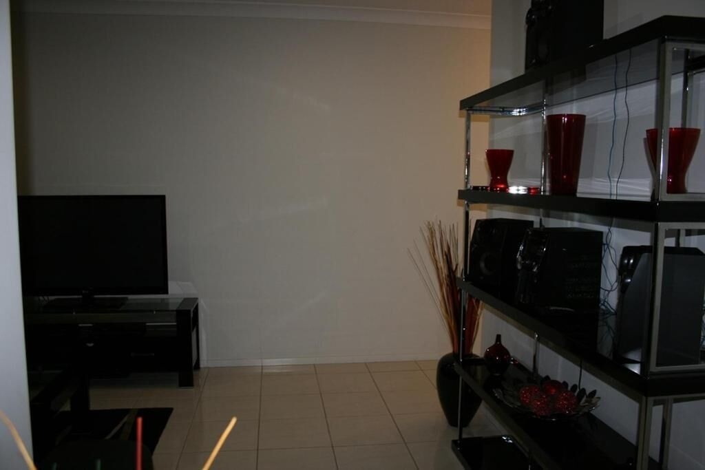 A modern living room with a flat-screen TV, a black entertainment unit, and a glass shelving unit with decorative items.