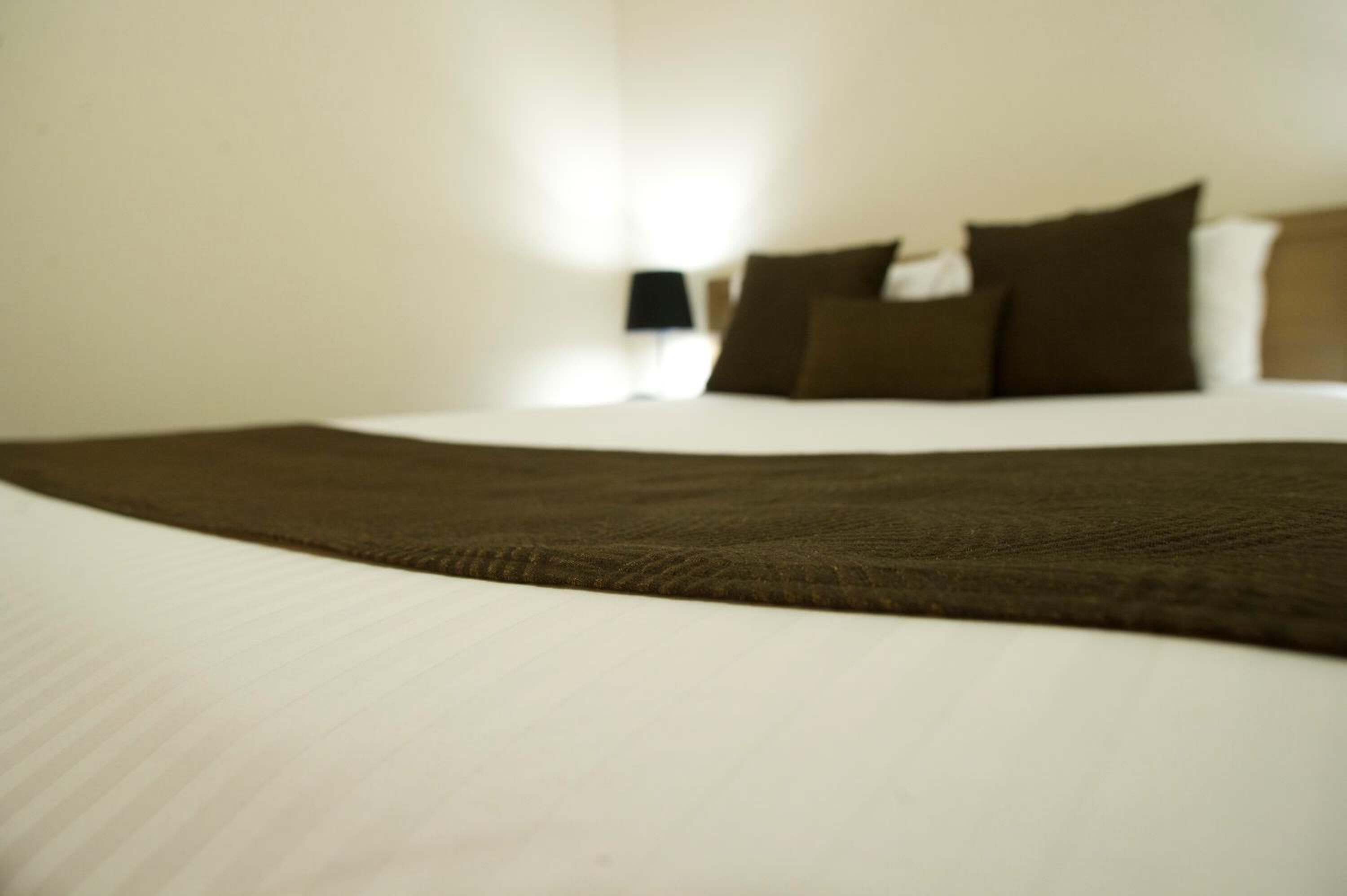 A neatly made bed with a brown blanket and white sheets, a bedside lamp, and several pillows on the headboard.