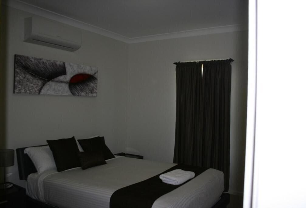 Een hotelkamer met een bed, nachtkastje, airconditioning en een raam met gordijnen.