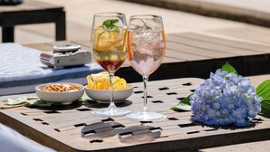 Deux verres de boissons glacées à la menthe et un petit bol de noix sur une table en bois, près d’une piscine.