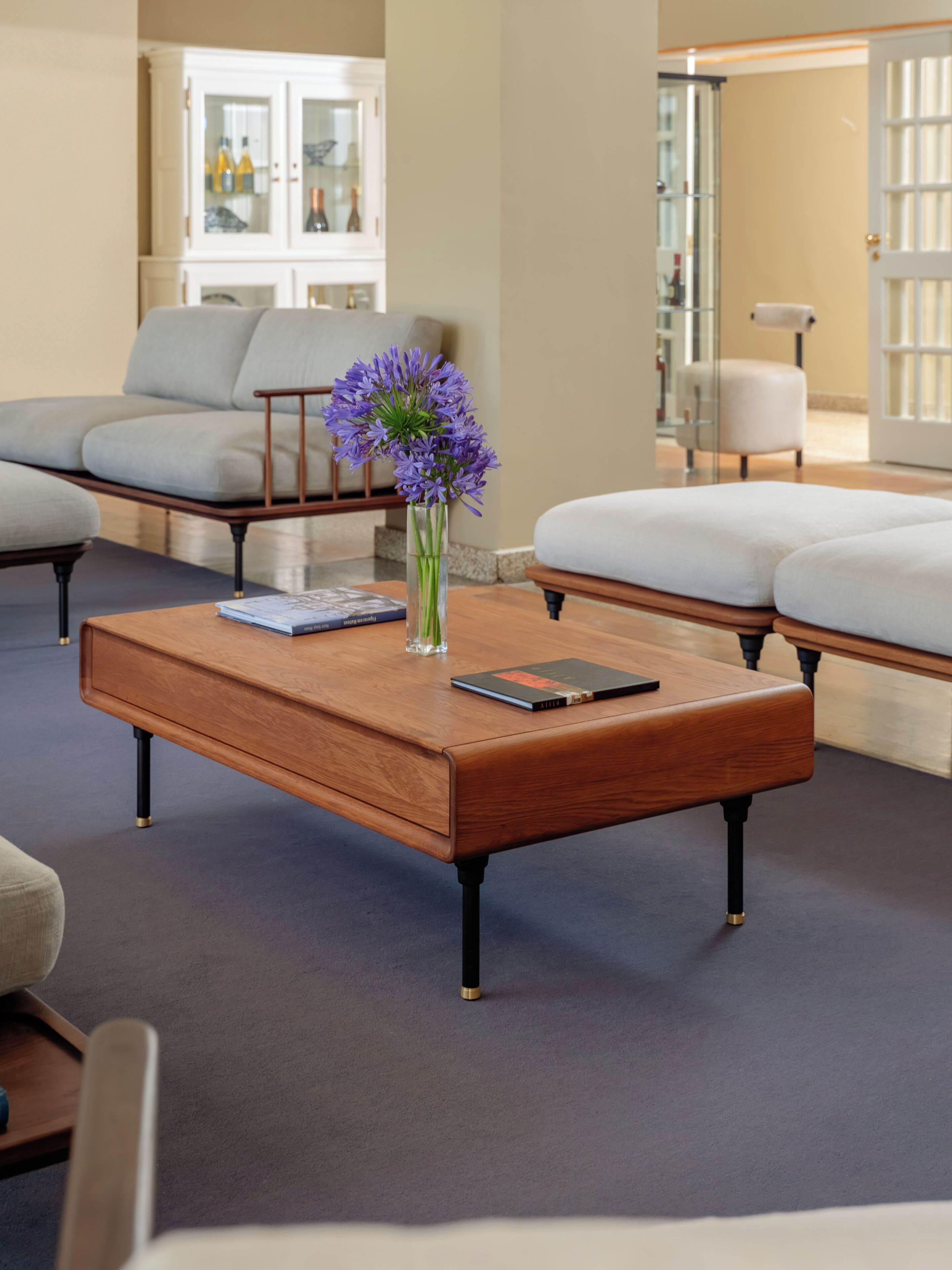 Un salon moderne avec une table basse en bois, un vase contenant des fleurs violettes et un livre.