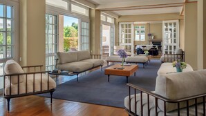 Un vaste espace de vie comprenant un canapé, un pouf et une table basse, de grandes fenêtres et une vue sur l’extérieur.