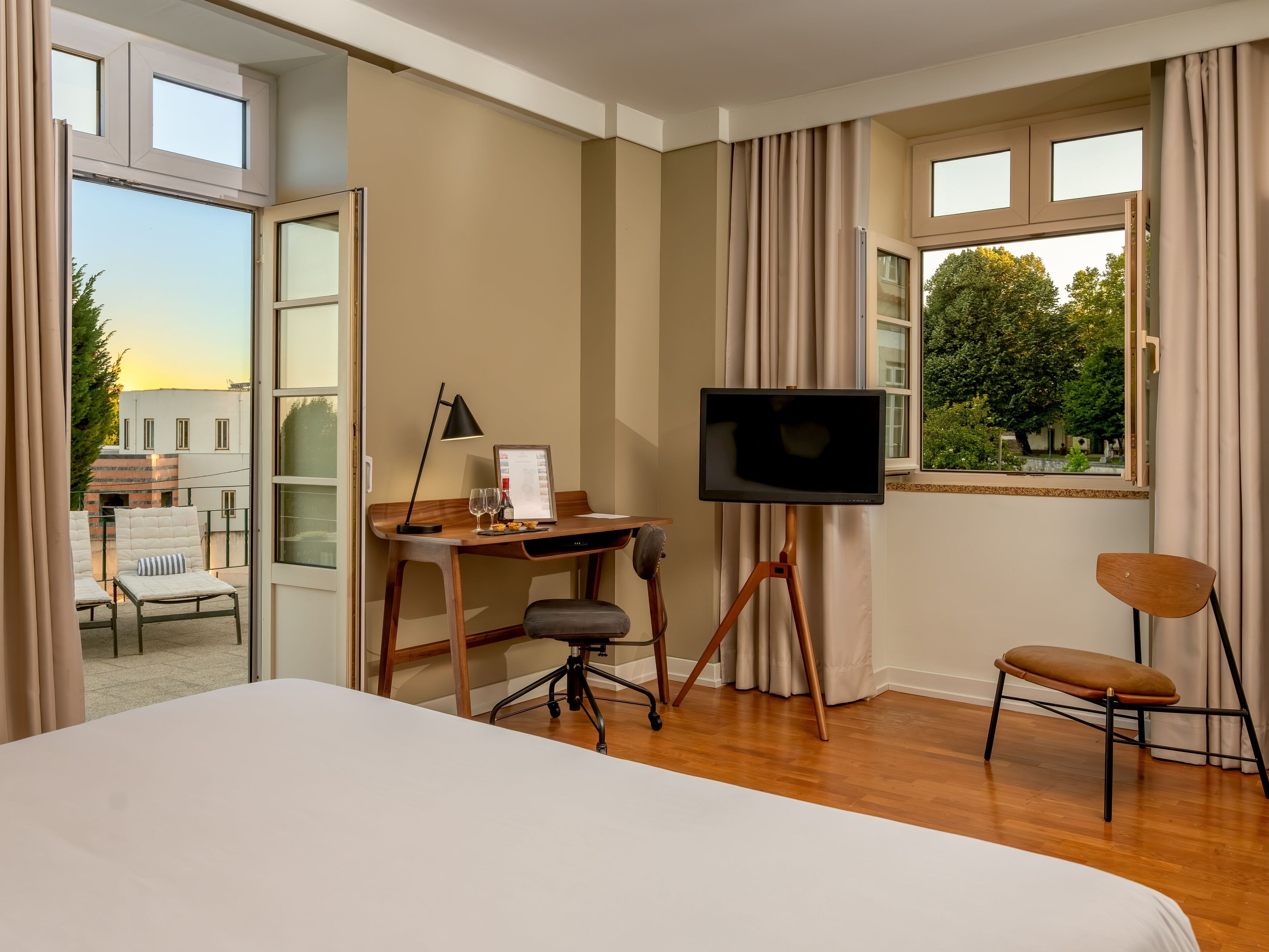 A hotel room with a bed, a desk with a computer, a TV, and a chair.