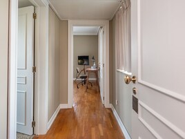 Un pasillo con suelo de madera, paredes blancas y una puerta a la derecha.