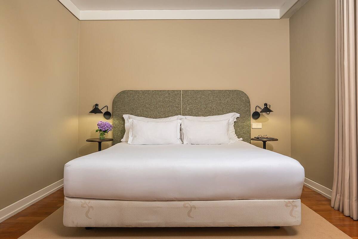 A neatly made bed with white linens, two bedside tables with lamps, and a headboard.