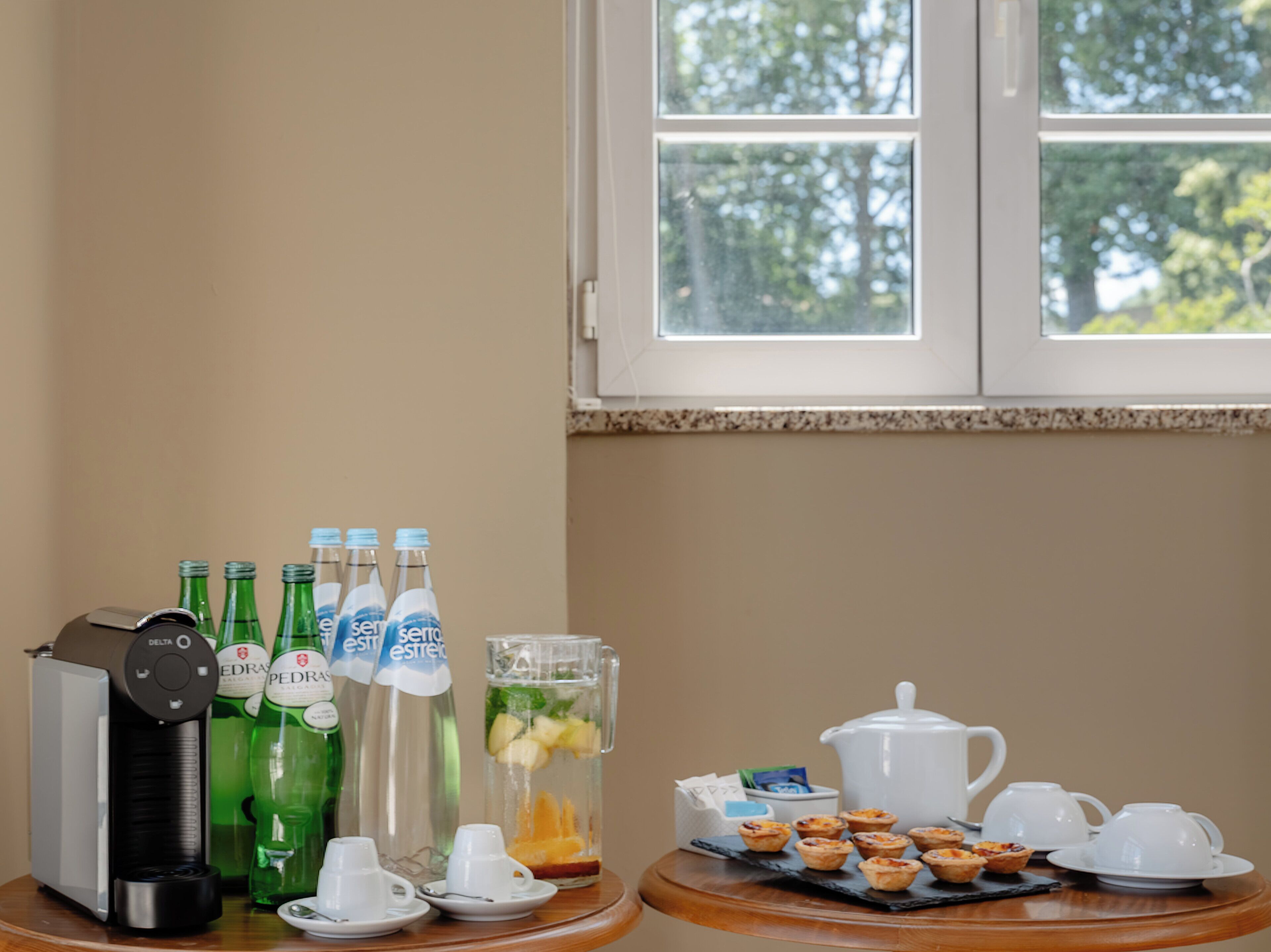 A breakfast setup with a coffee maker, bottled water, a pitcher with fruit, and tea service on a table.