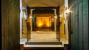 Entrada de hotel con puerta de vidrio, piso de mármol y una planta en maceta.