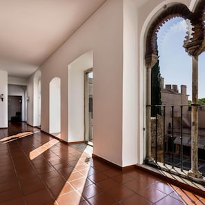 A corridor with tiled flooring, white walls, and a view through an arched window.