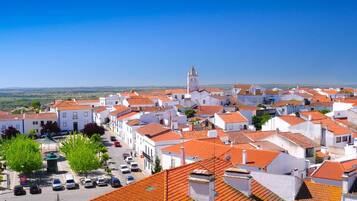 A town with white buildings and red roofs, a clear sky, and a distant view of the sea.