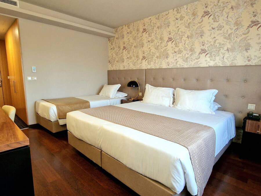 A hotel room with two beds, a wooden desk, a small table, and a nightstand with a lamp.