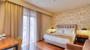 Habitación de hotel con una cama grande, un escritorio de madera, una silla y una mesita de noche con lámpara.