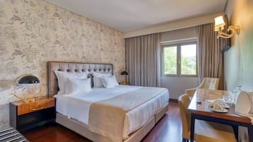 A hotel room with a large bed, a bedside table with a lamp, a desk with a chair, and a window with curtains.