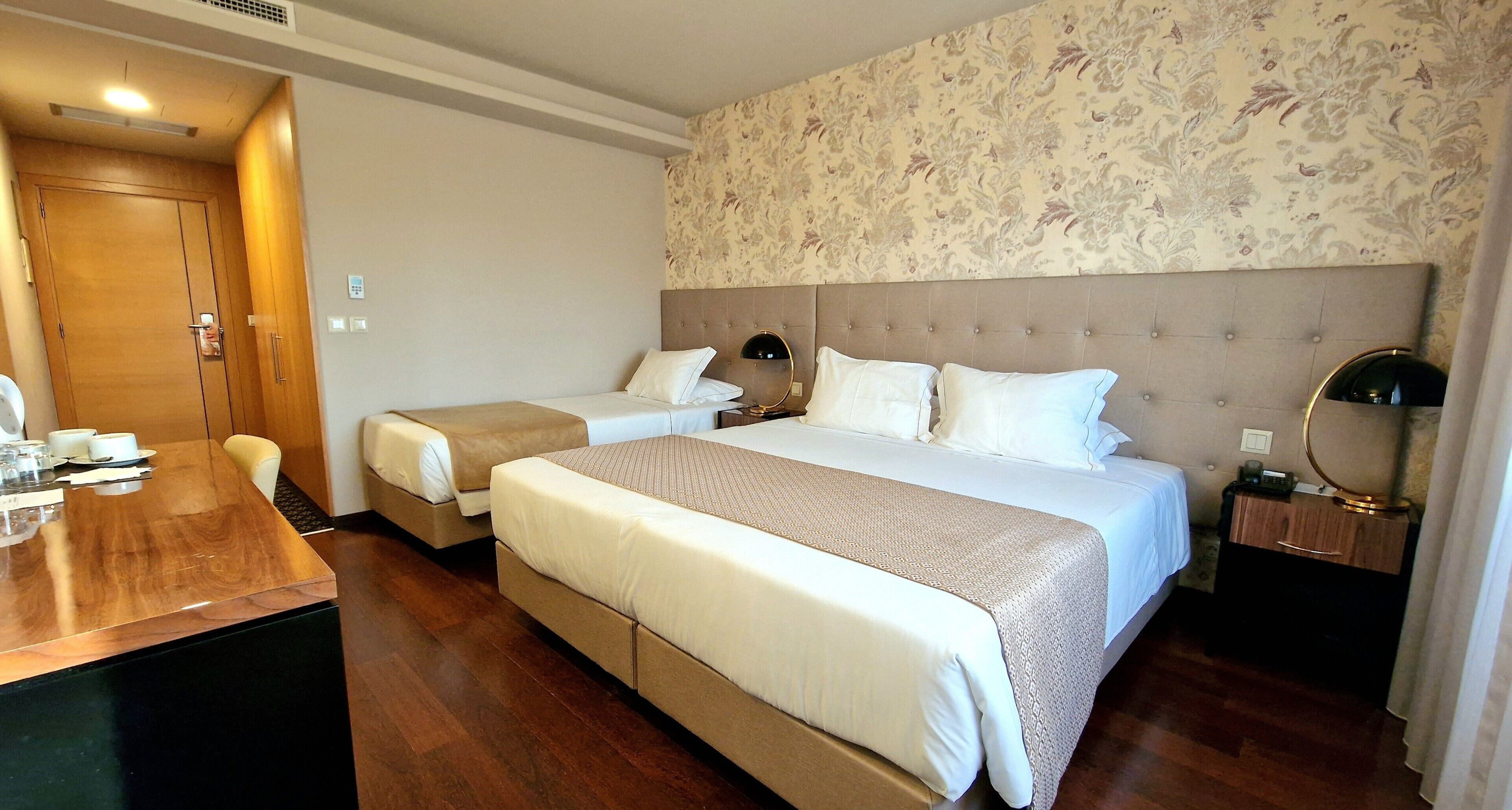 Een hotelkamer met twee bedden, een houten bureau, een klein tafeltje en een nachtkastje met een lamp.