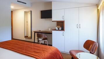 A hotel room with a bed, a desk, a chair, a television, and a wardrobe.