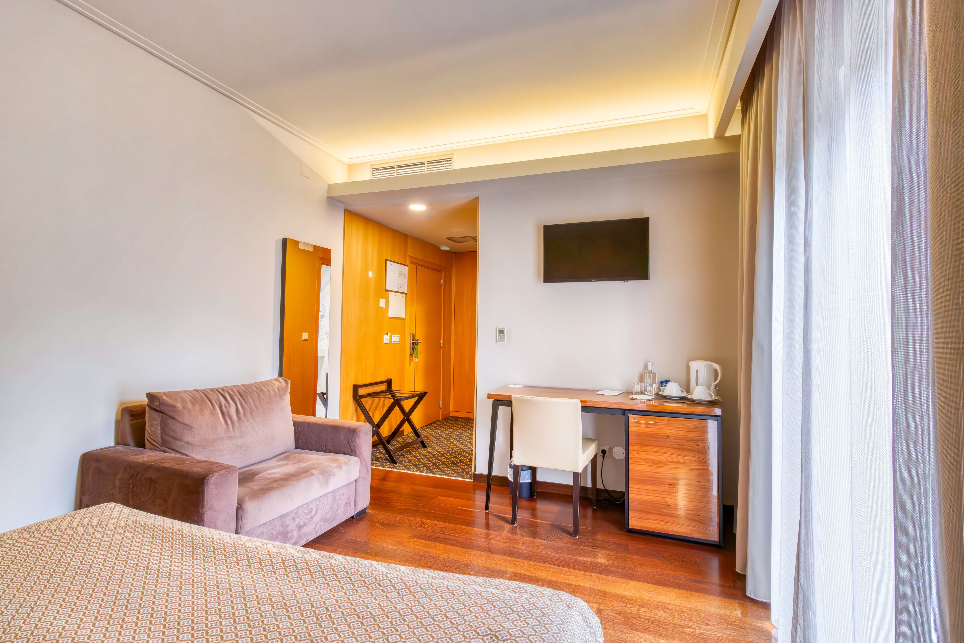 A hotel room with a bed, a sofa, a desk, and a television.