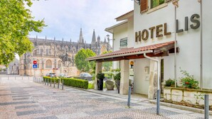 A hotel named "HOTELLIS" with a cobblestone street in front, a stop sign, and a historic cathedral in the background. - Hotel Lis Batalha (Batalha)