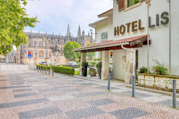 Un hotel llamado "HOTELLIS" con una calle adoquinada al frente, una señal de parada y una catedral histórica al fondo.