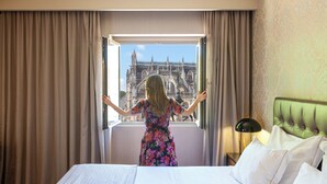 A hotel room with a large window, a bed, a nightstand with a lamp, and a green upholstered headboard. - Hotel Lis Batalha (Batalha)