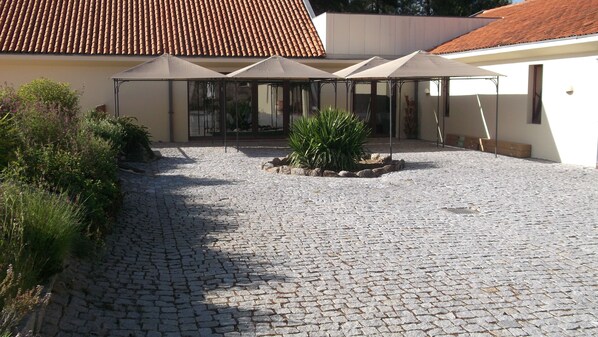 A courtyard with cobblestone paving, a covered seating area with umbrellas, and a building with a tiled roof. - Pousada Convento De Belmonte (Belmonte)