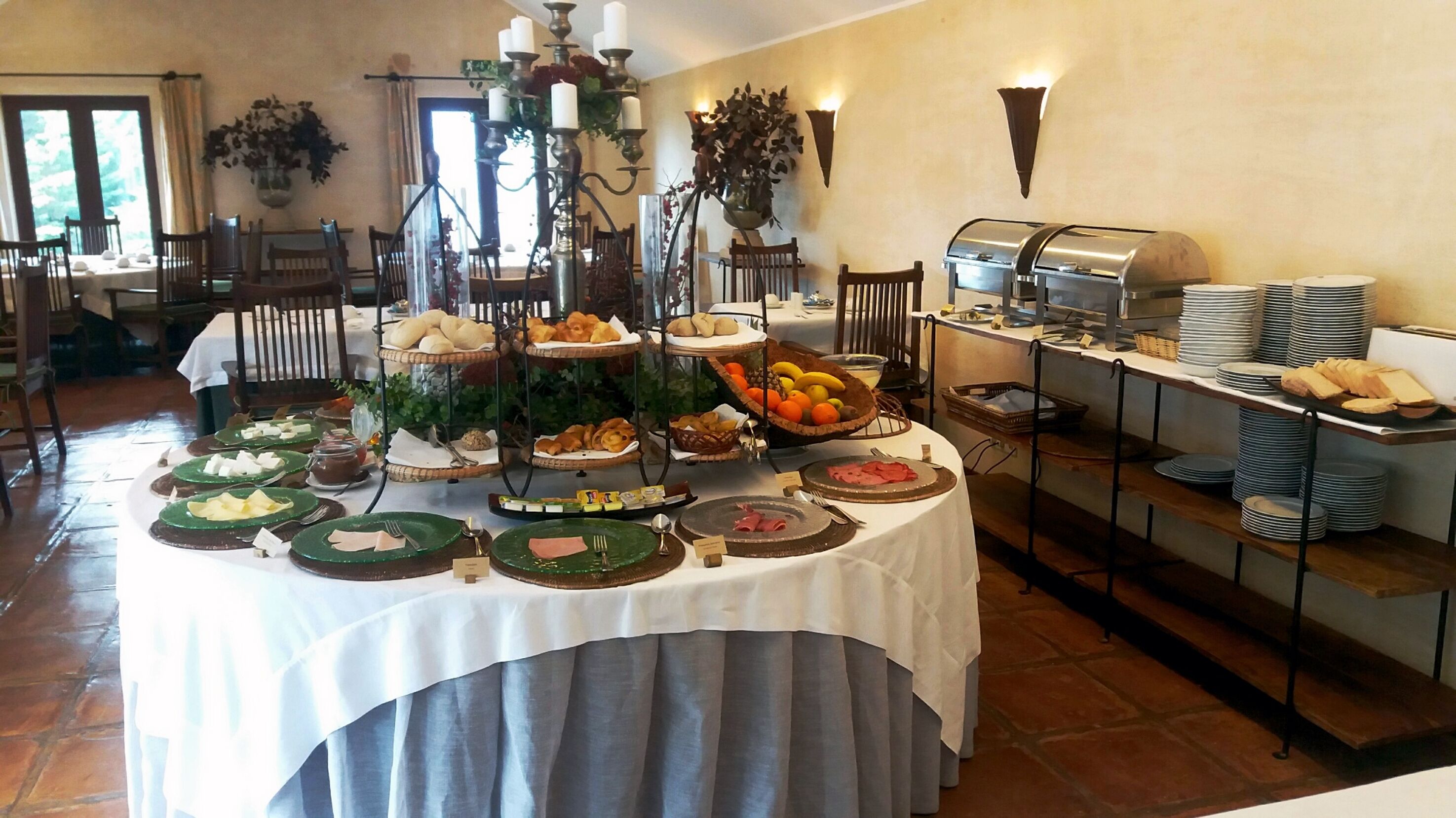 A buffet setup with various food items, including fruits, pastries, and meats, arranged on a table with a white tablecloth.