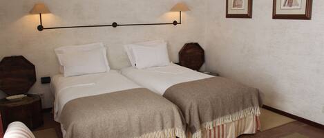 A double bed with two pillows, a bedside table, a chair, and a small table with a notebook.