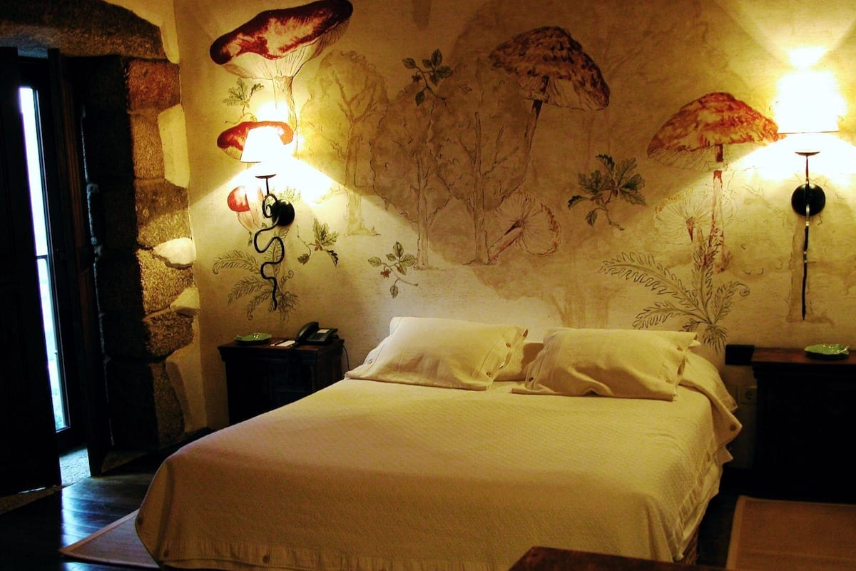A bedroom with a large bed, two bedside lamps, a telephone, and a wall mural.
