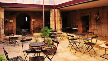 Enjoy dining and socializing in this spacious patio area with tables and chairs, surrounded by lush greenery and a high ceiling.