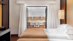 A hotel room with a bed, a desk, a chair, and a view of a balcony with a table and chairs. - Pousada Forte Horta (Horta)