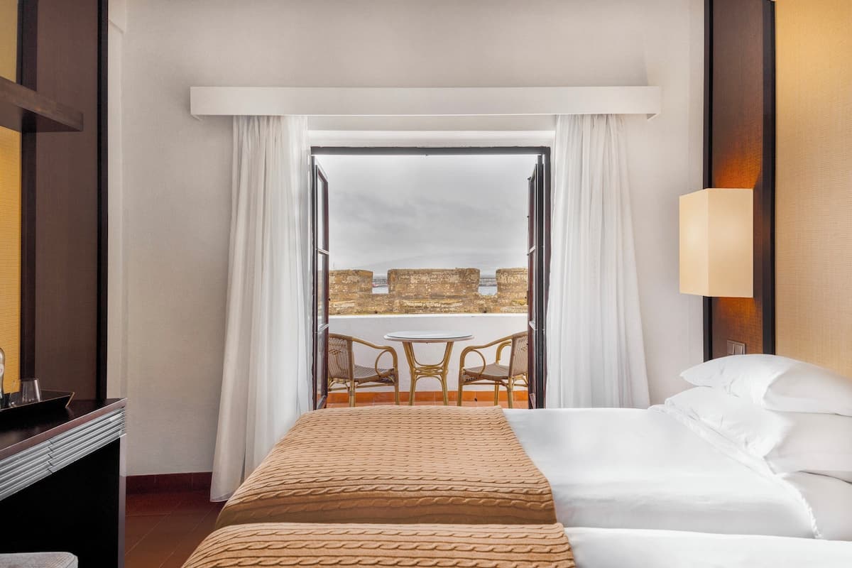 A hotel room with a bed, a desk, a chair, and a view of a balcony with a table and chairs.