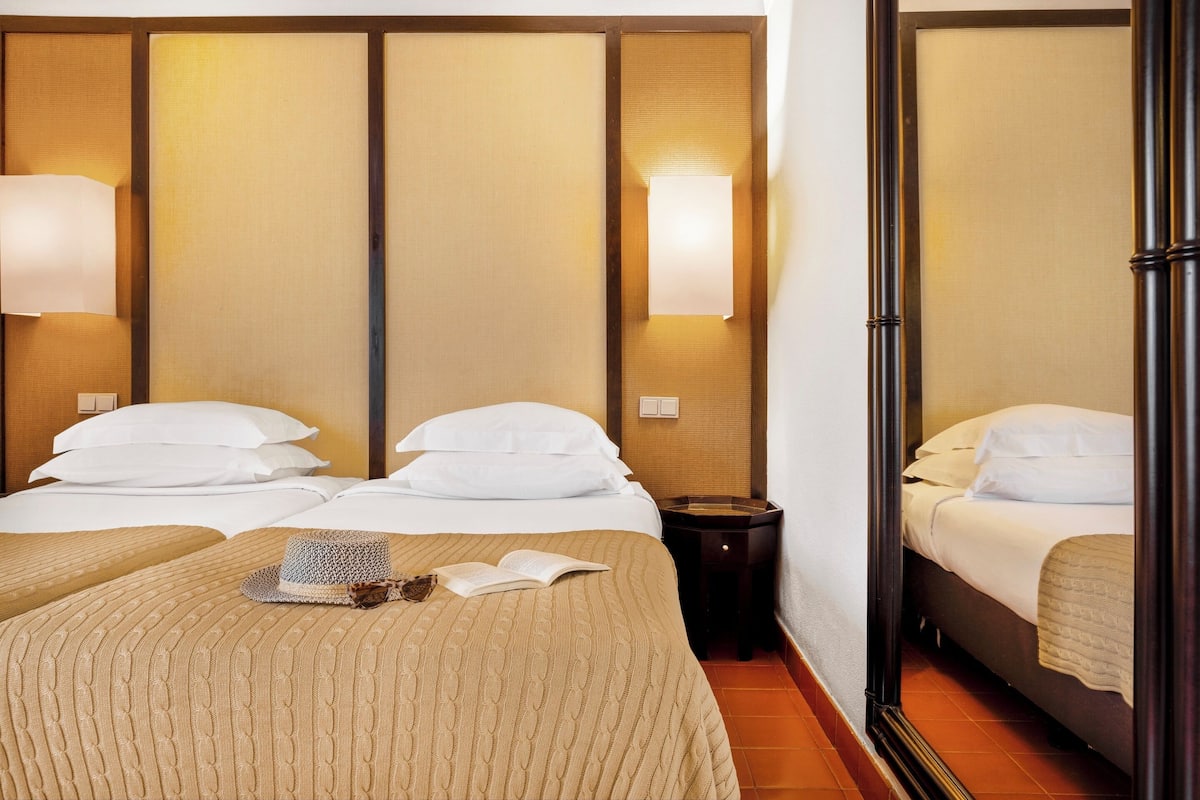 A hotel room with two beds, a bedside table, a lamp, and a mirror.