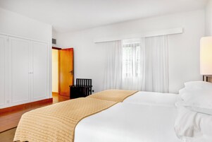 Una habitación de hotel con una cama grande, un armario, un escritorio y una ventana con cortinas.