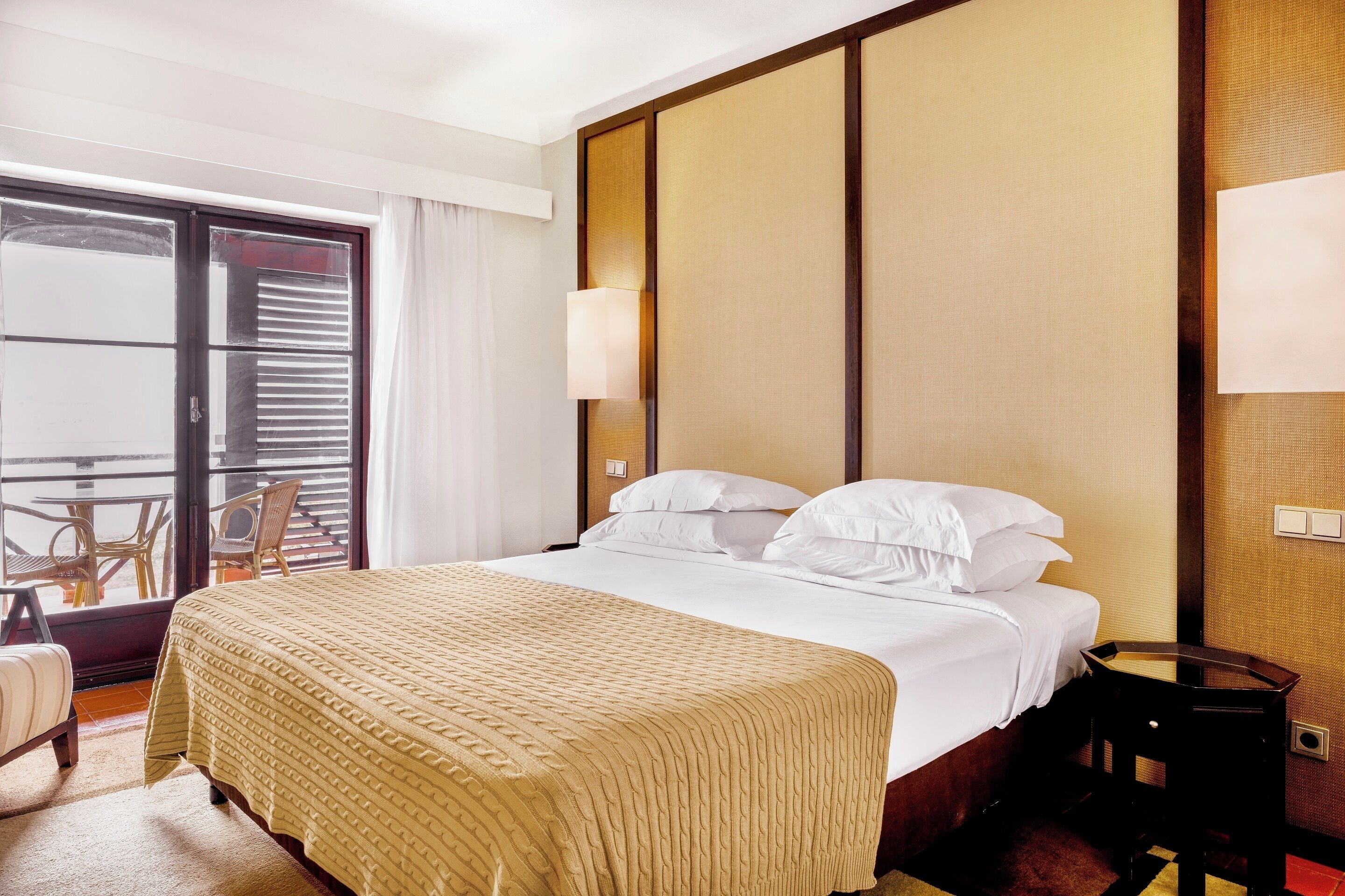 A hotel room with a bed, a nightstand, a chair, and a view of the outside balcony.