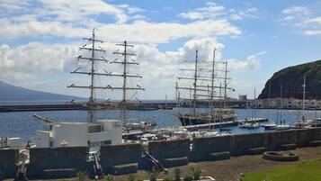 A harbor with two tall ships docked, a white building with a sign, and a mountainous backdrop.