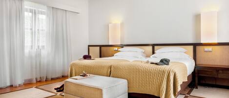 A hotel room with a bed, bedside tables, a nightstand, a window with curtains, and a pair of shoes on the floor.