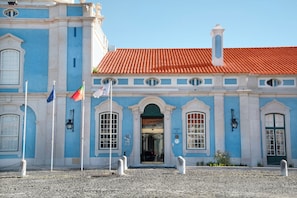 A building with a blue facade, red-tiled roof, and multiple flags. - Pousada Queluz (Sintra)