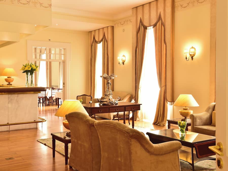 A hotel room with a dining area, a sofa, a table with a vase, and a lamp.