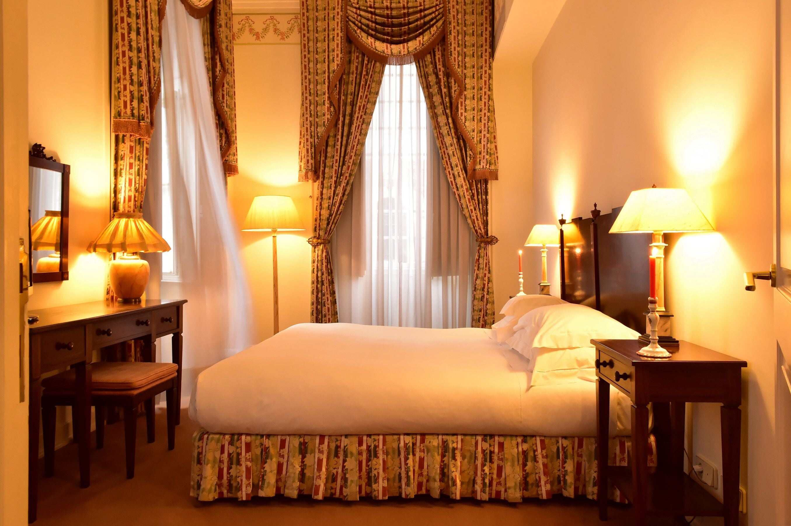 A hotel room with a bed, a desk, a chair, a nightstand, and two lamps.