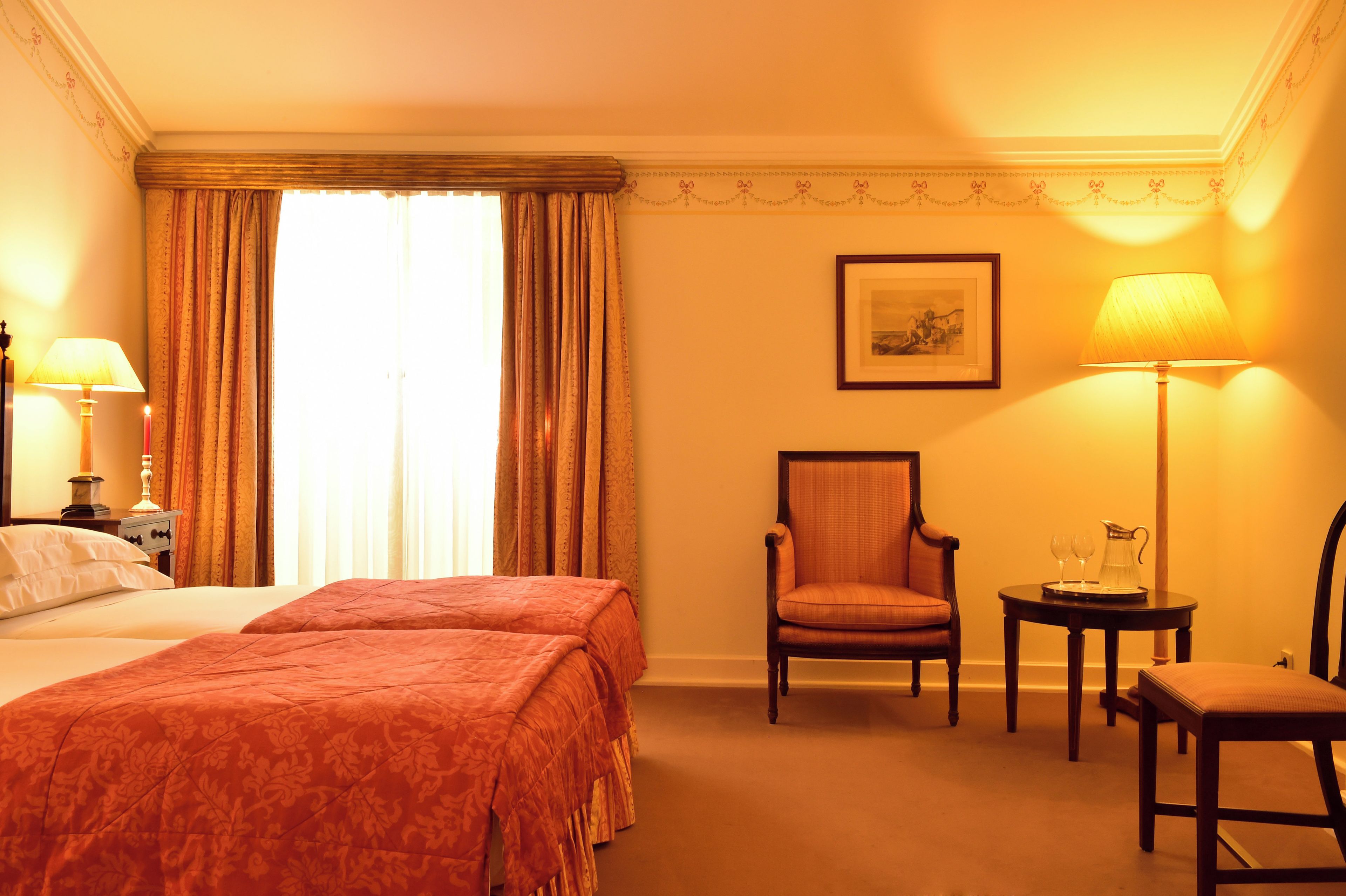 Habitación de hotel con una cama, dos sillas, una mesa con jarrón y un cuadro en la pared.