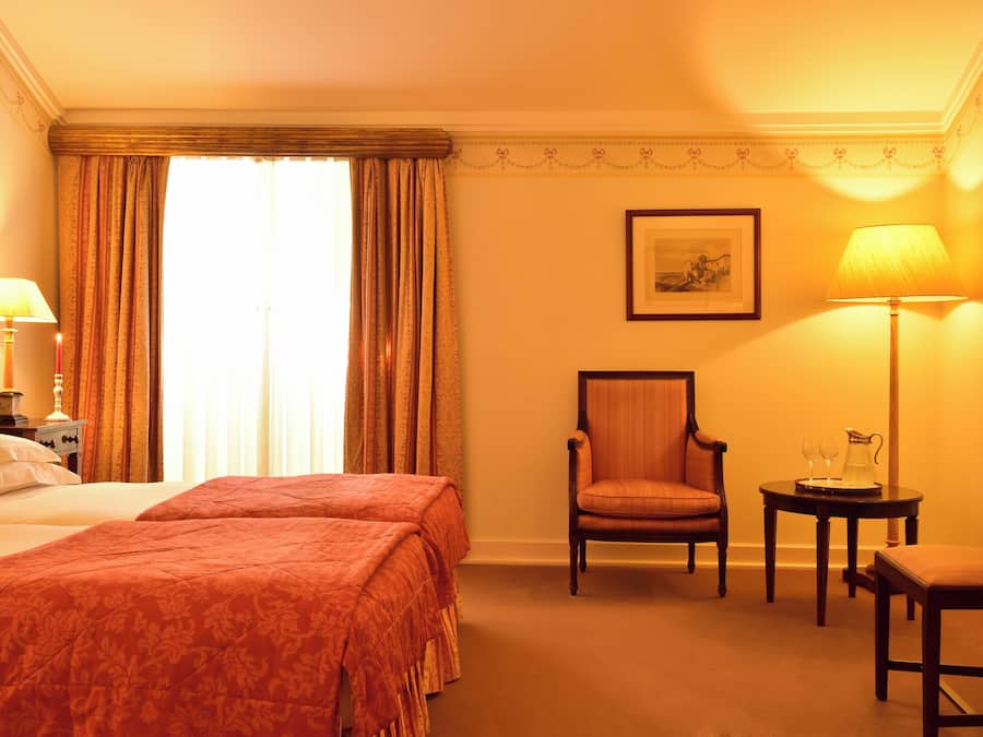 A hotel room with a bed, two chairs, a table with a pitcher, and a framed picture on the wall.