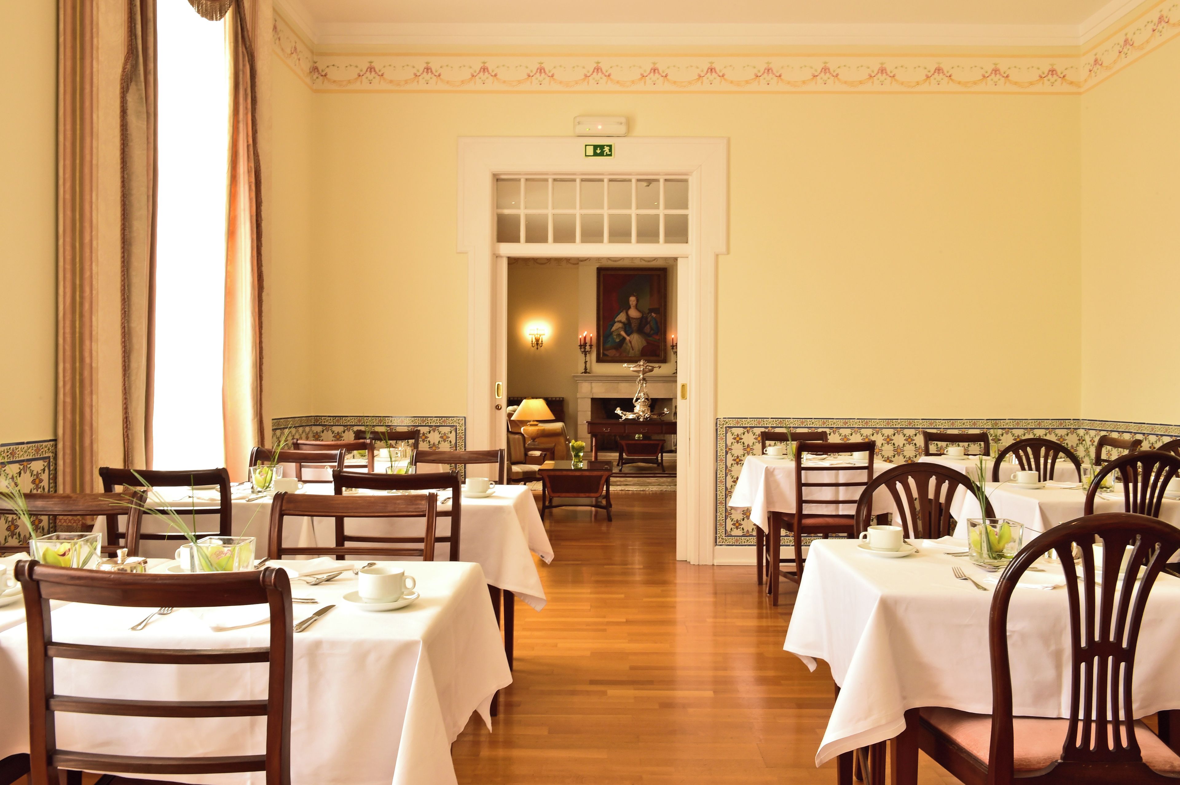 A dining area with tables set for service, a chandelier, and a painting on the wall.