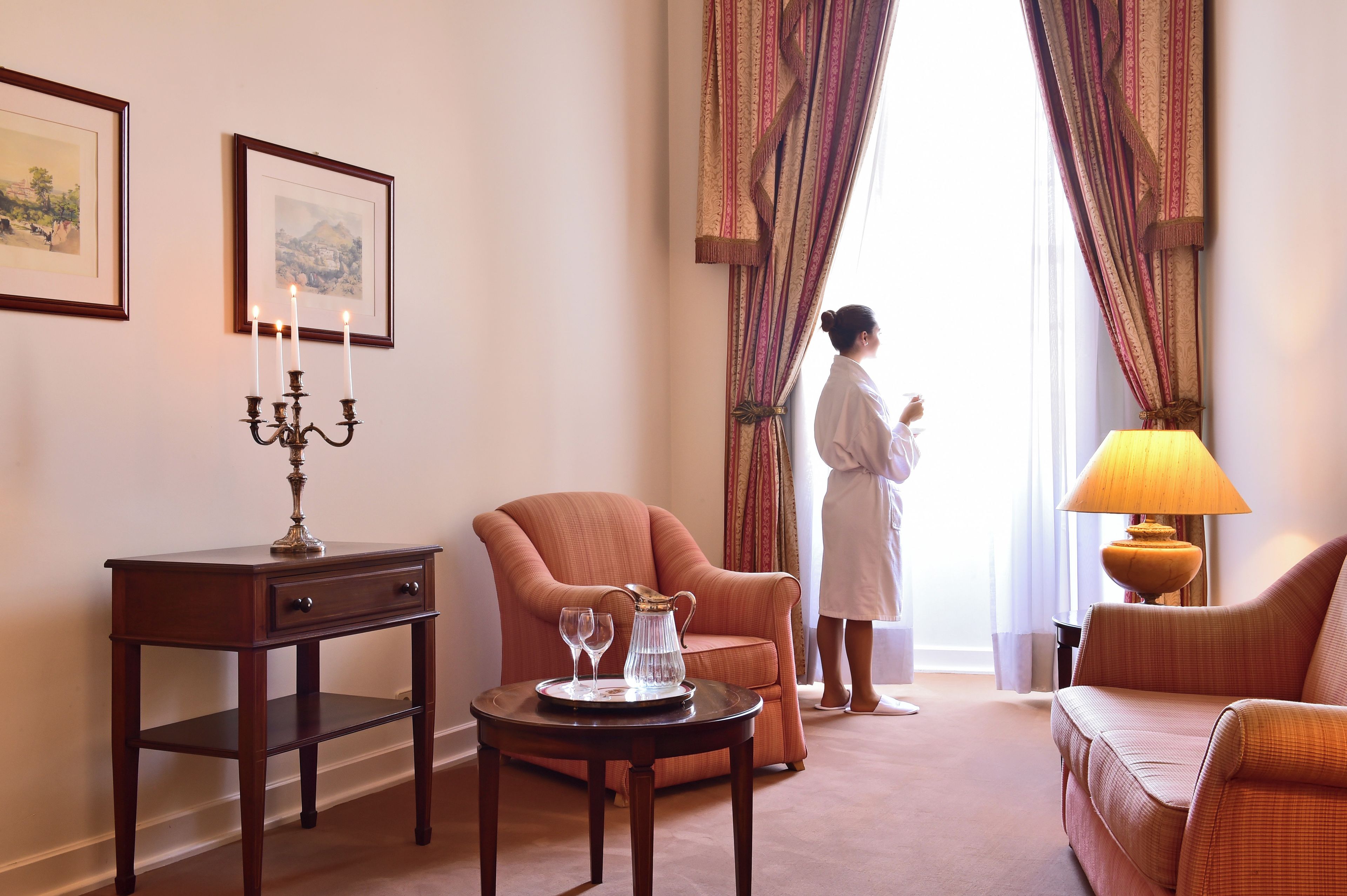 Une chambre d’hôtel avec un coin salon, une table avec une bougie, une lampe et une vue sur l’extérieur.