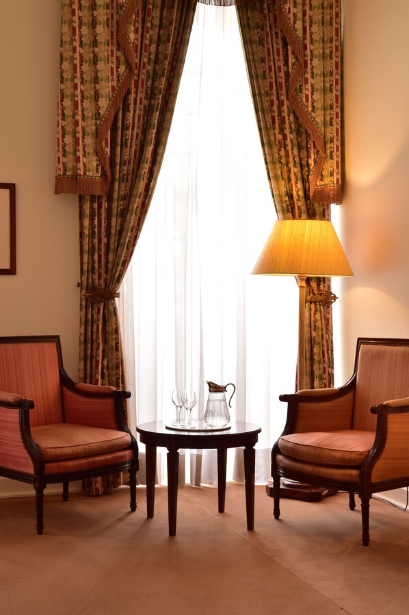 Una habitación con dos sillas de madera, una mesita con una jofaina y un vaso, y una lámpara.