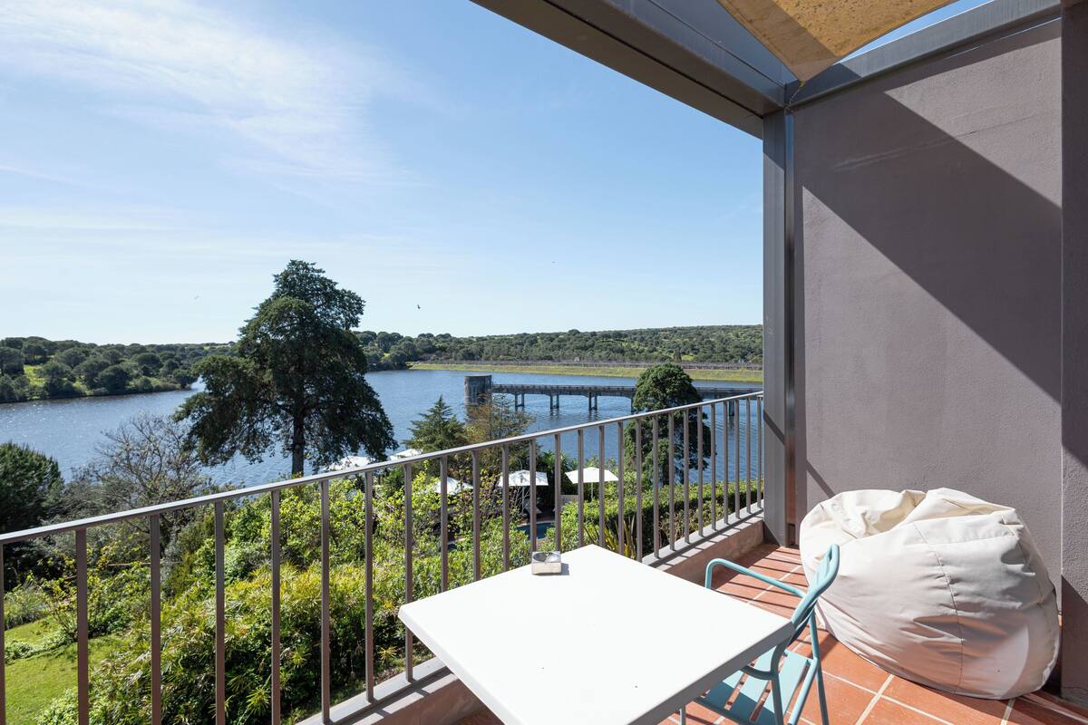 A balcony with a table and chairs, overlooking a lake and forest.