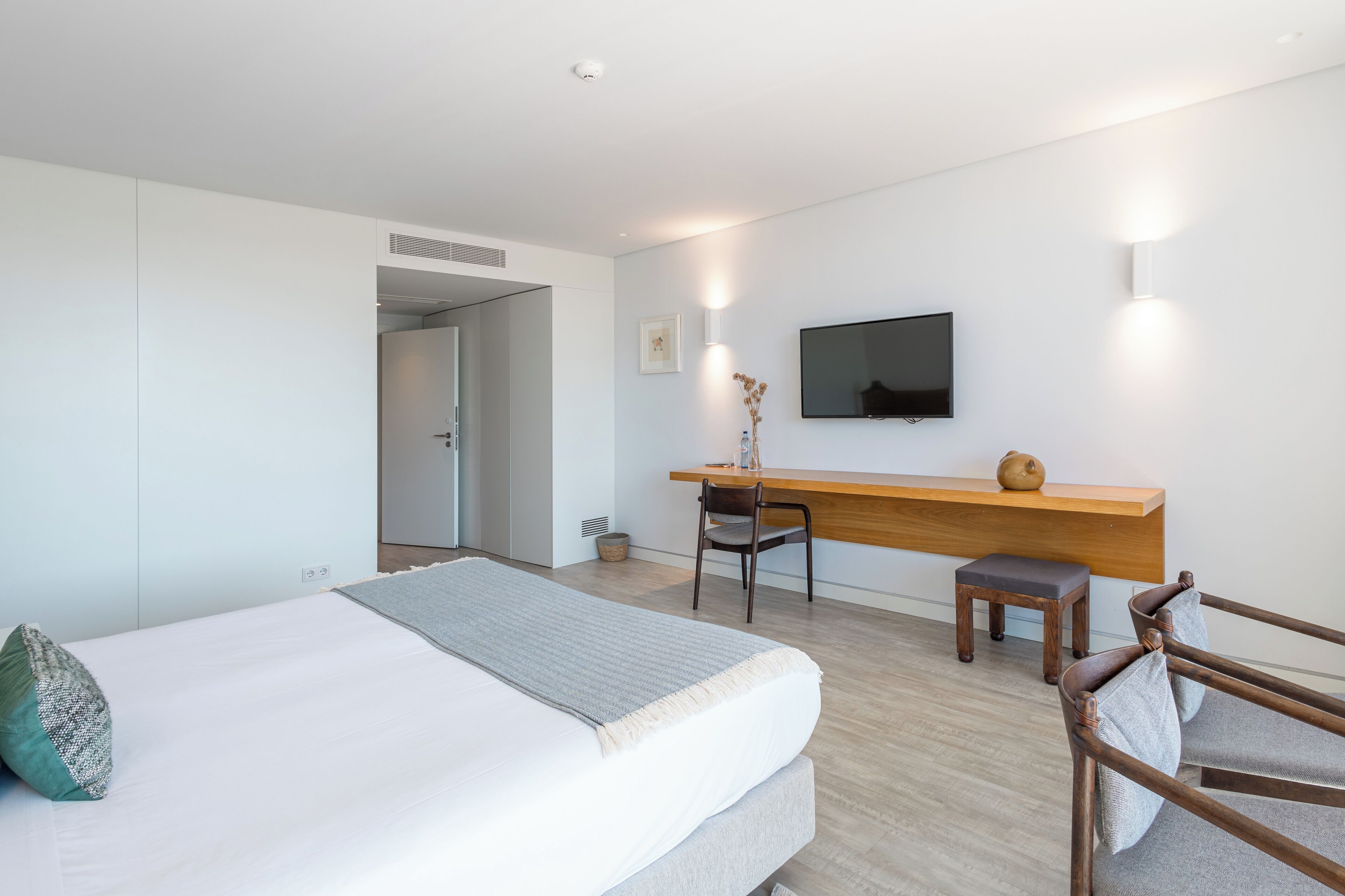 A modern hotel room with a bed, a desk, a chair, and a TV.