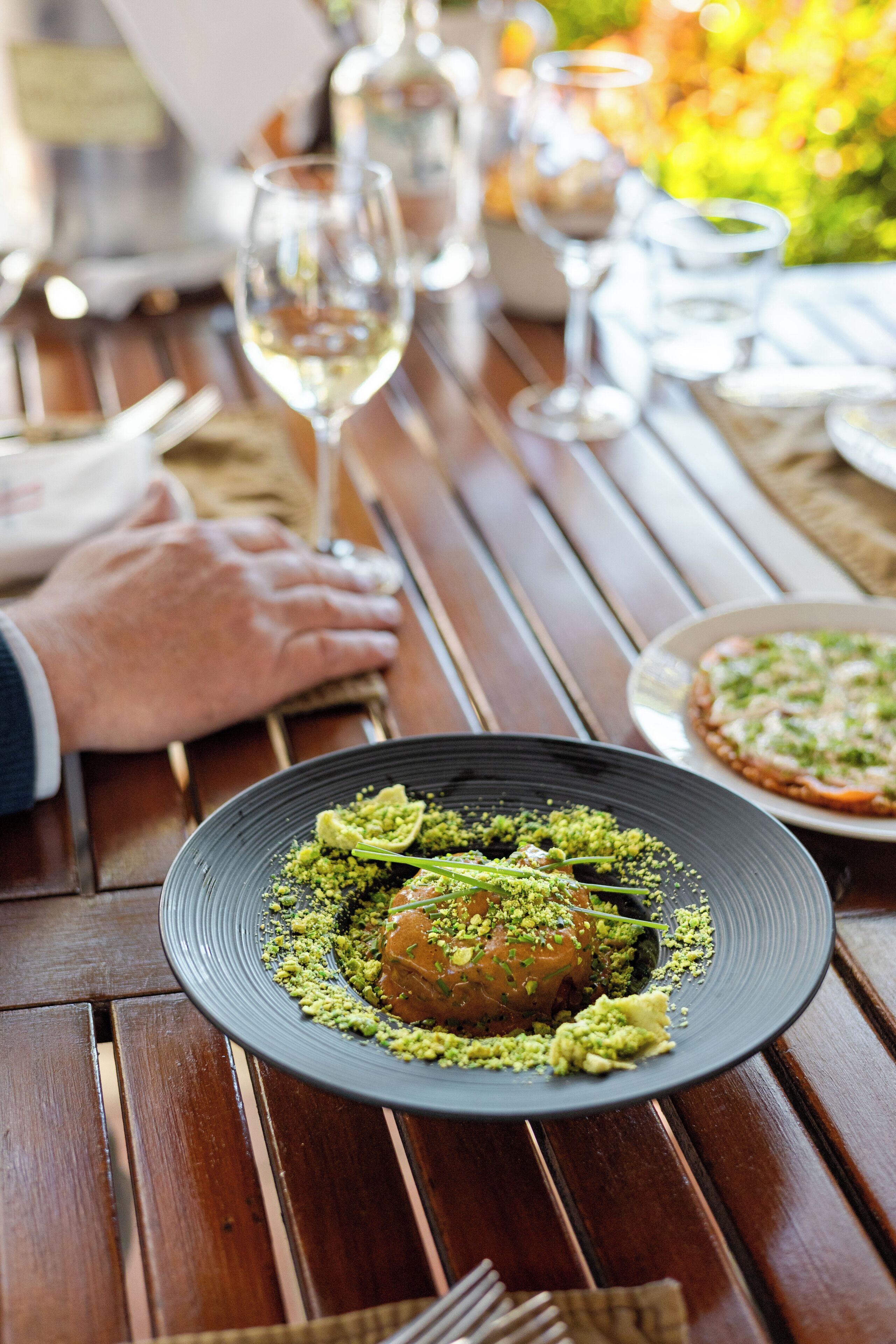 A dining table with a plate of food, glasses of wine, and a person's hand resting on the table.