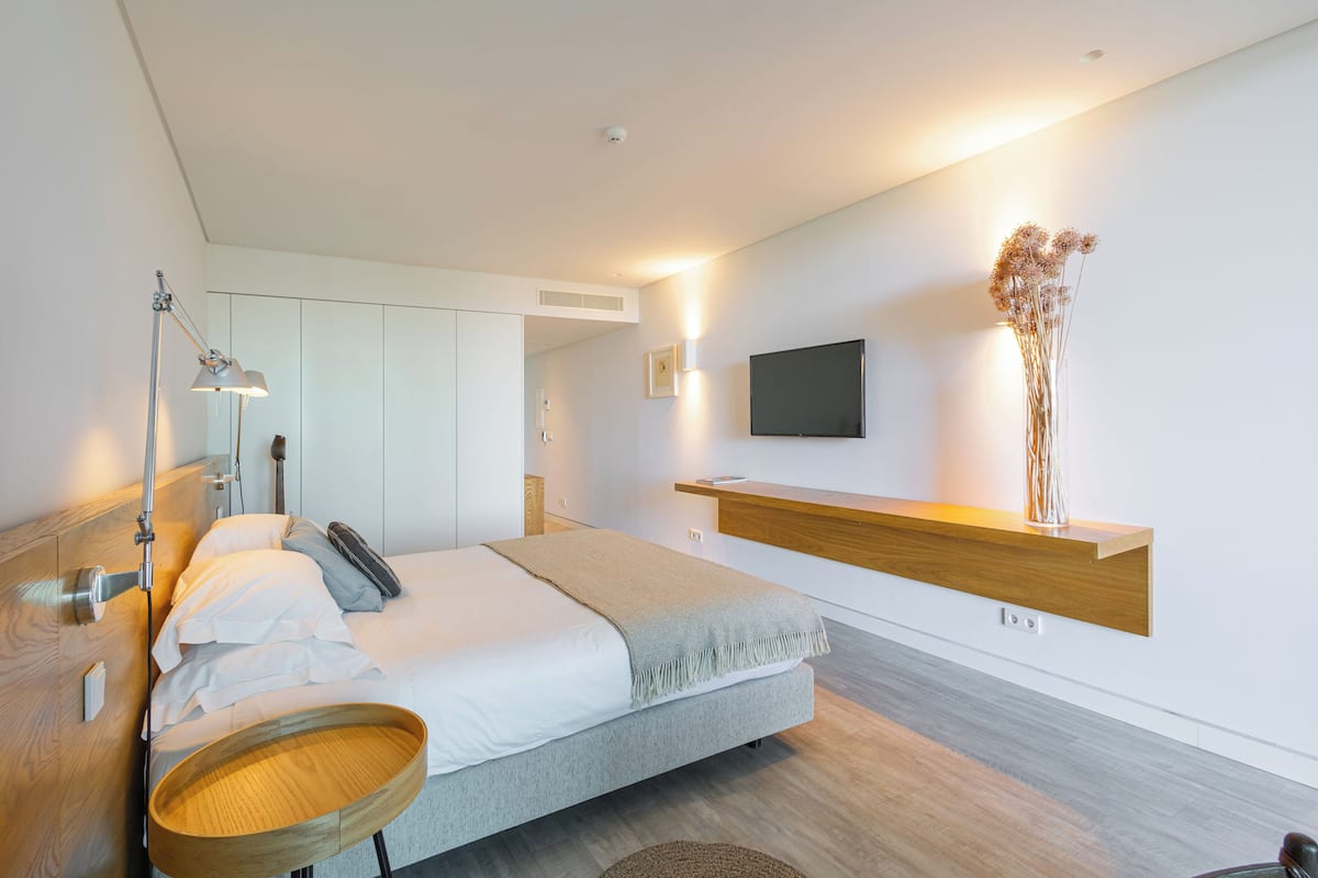 A modern bedroom with a bed, bedside table, lamp, and a mounted TV.