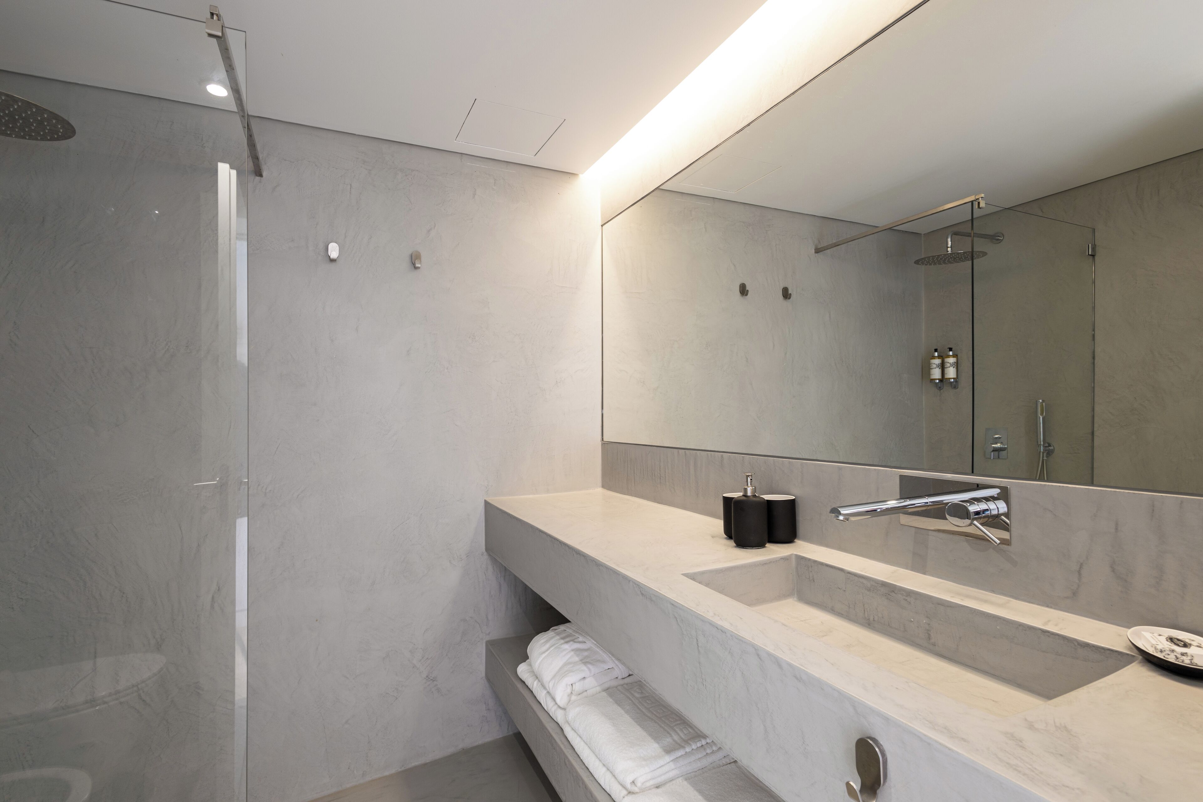 A modern bathroom with a large mirror, a marble sink, and a glass-enclosed shower.