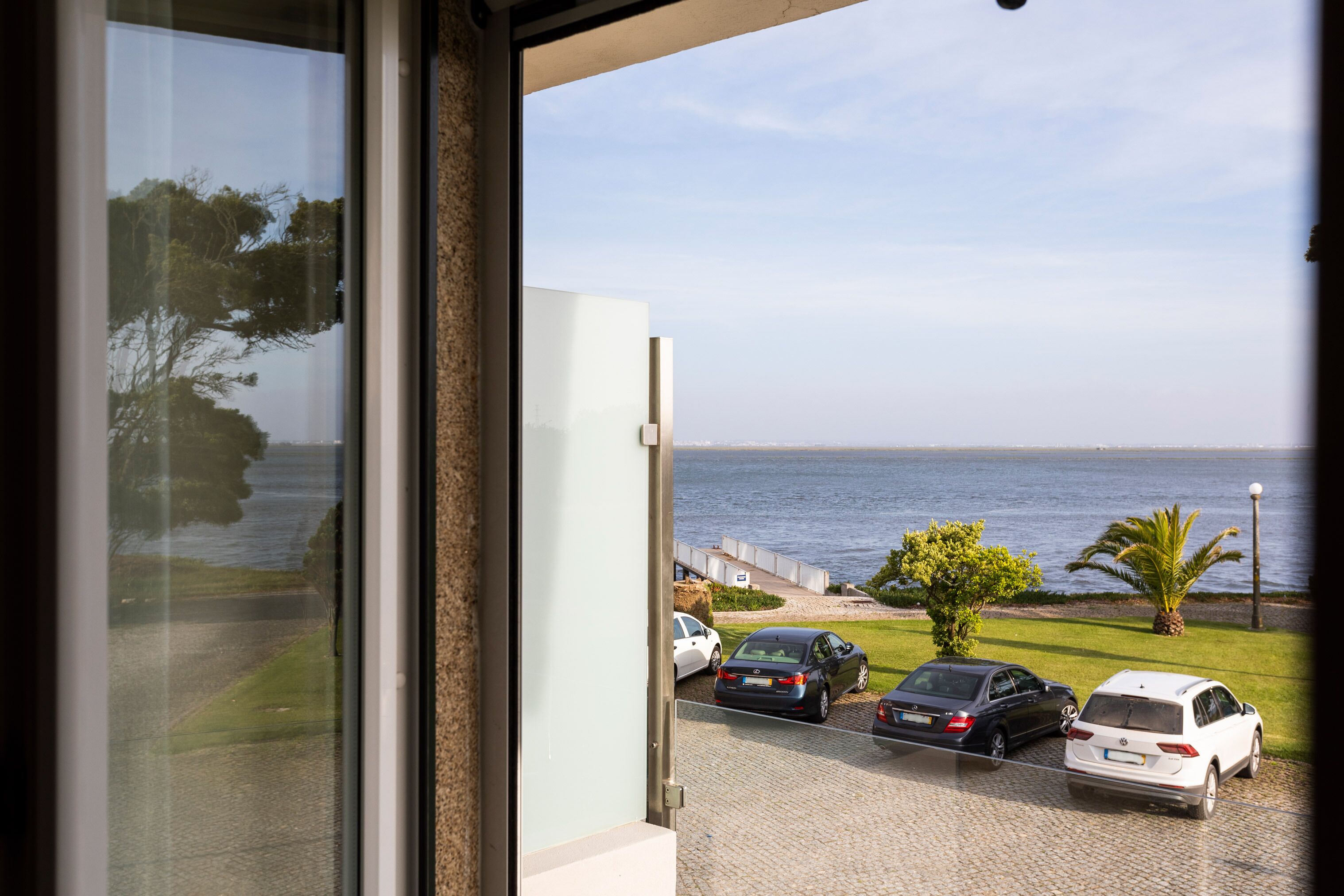 A view from a balcony overlooking a parking area with cars and a body of water.